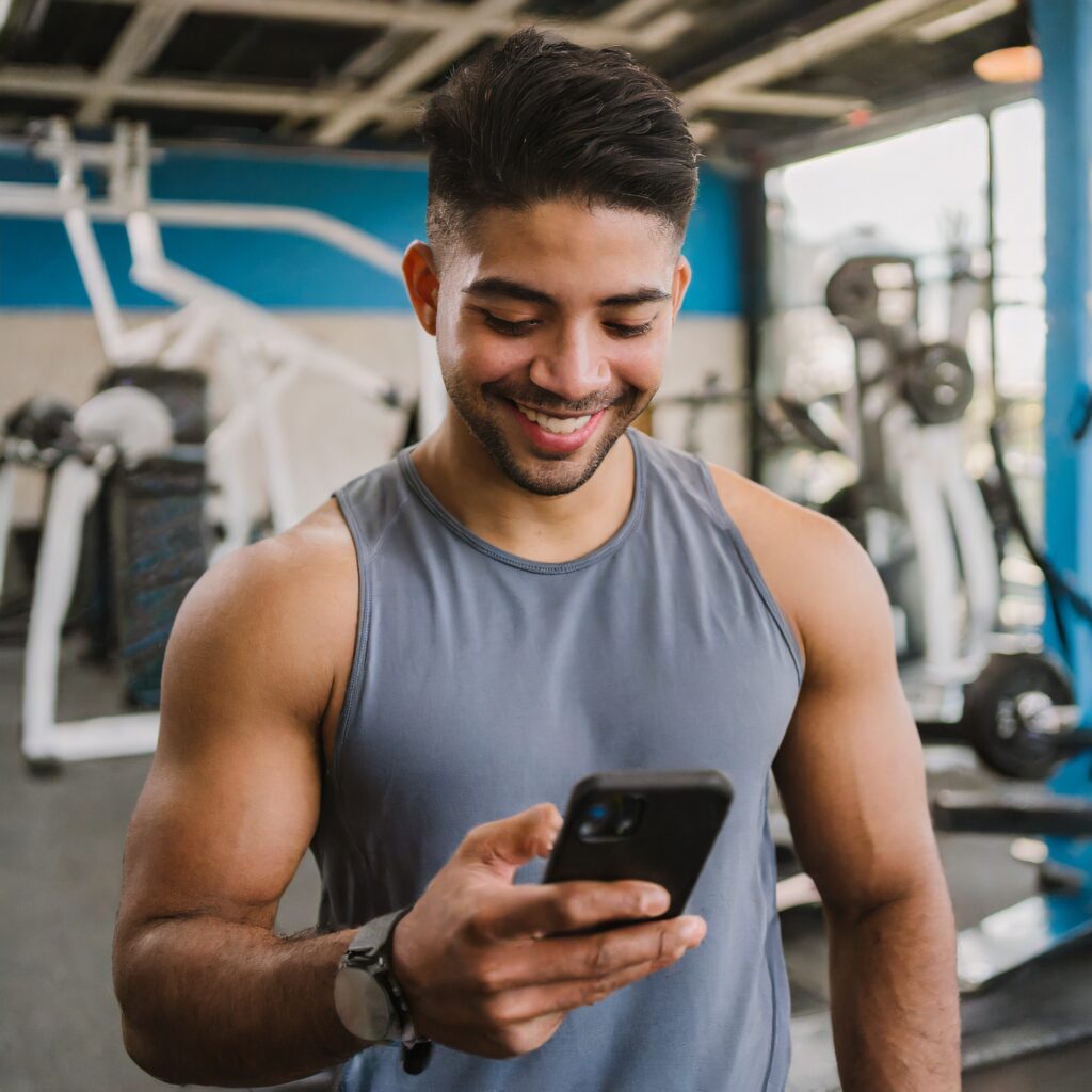 Man at Gym Looking At Phone. Following an online coaching program.